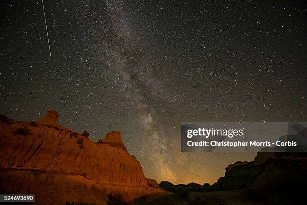 The Milky Way galaxy appears in the dark night sky with shooting stars over hoodoos in the Alberta Badlands at Dinosaur Provincial Park.