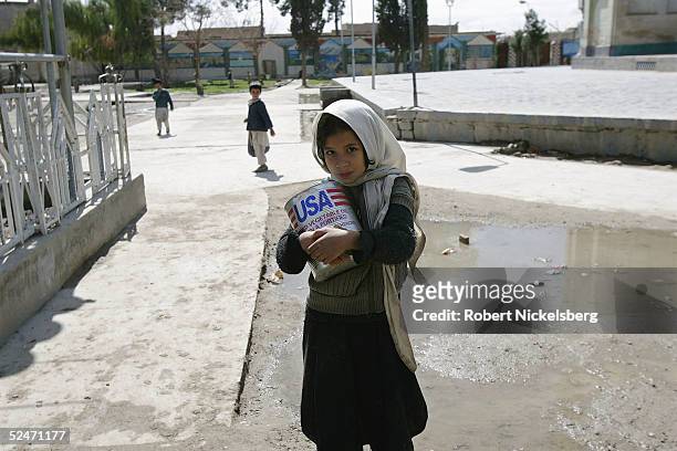 An Afghan girl carries a can of US AID donated cooking oil home from school through the memorial tomb of Pashtun leader Ahmad Shah Baba March 1, 2005...