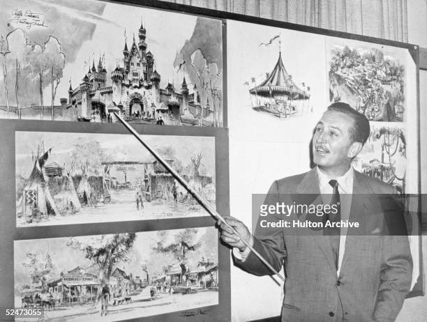 American producer, director, and animator Walt Disney uses a baton to point to sketches of Disneyland, 1955.
