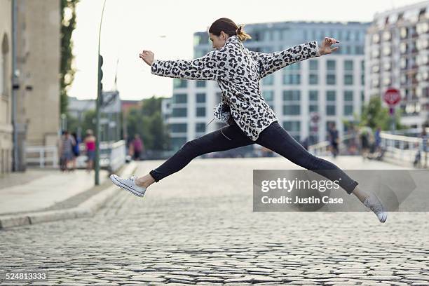 woman making a big jump in a sunny city street - leggings fotografías e imágenes de stock