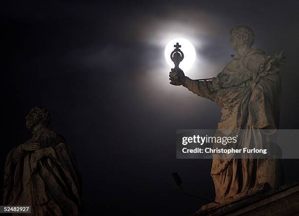 Full moon appears behind the statues that stand atop the collonade of St Peter's Square as Catholics take part in the Easter Vigil inside the Vatican...