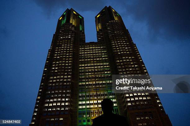 Man looks The Tokyo Metropolitan Government Building illuminated in the color of the Brazilian flag on April 27, 2016 in Tokyo, Japan. The landmarks...