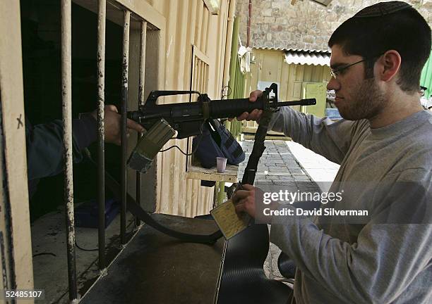 An Israeli settler hands his assault rifle to a policeman before entering the Cave of the Patriarchs during Purim festivities March 27, 2005 in the...