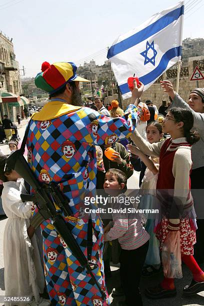 Armed Israeli settler Victor Atiya wears a clown suit as he gives children balloons during Purim festivities March 27, 2005 in the West Bank town of...