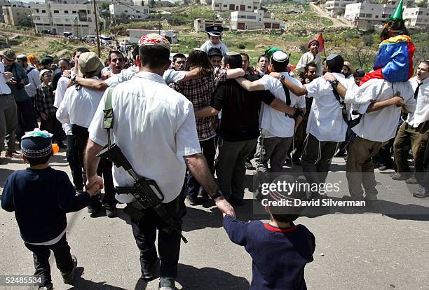 An armed Jewish settler joins in with his sons as others dance on their way to the Cave of the Patriarchs during Purim festivities March 27, 2005 in...