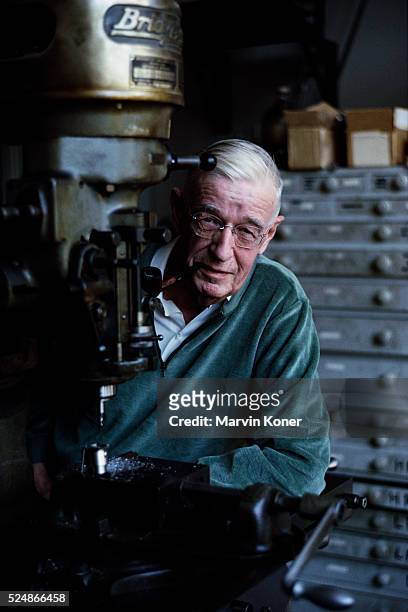 American engineer and inventor Vannevar Bush smoking a pipe as he poses at a drill press, circa 1960.