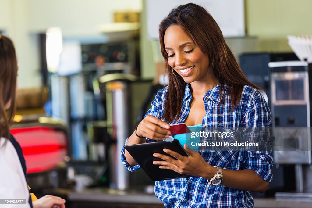 Coffee shop cashier swiping card on digital tablet reader