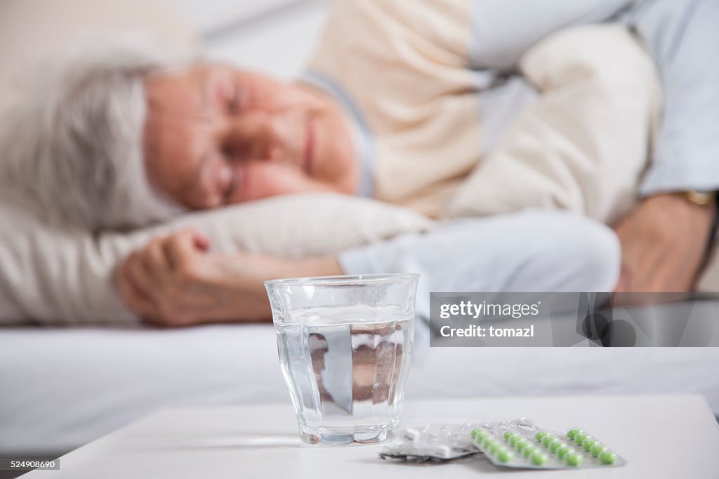 Pills on a night table and senior woman sleeping