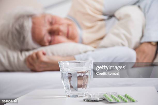 pills on a night table and senior woman sleeping - woman sleeping table stock pictures, royalty-free photos & images