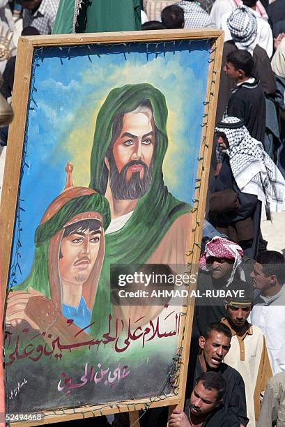 Shiite Muslim pilgrim hold up a large banner depicting the Imam Hussein and Imam Ali 30 March 2005, in the holy city of Karbala, 100 kms south of...