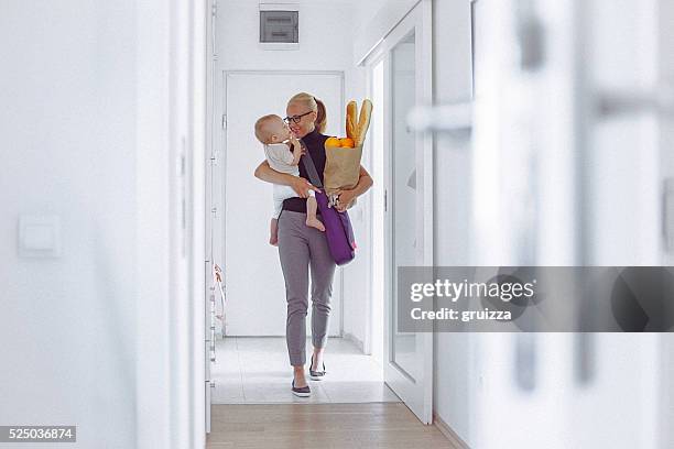 young mother enters home, carrying her baby and grocery bag - baby bag bildbanksfoton och bilder