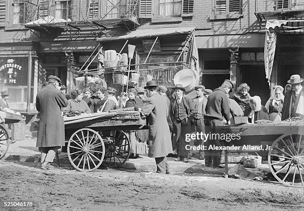 Photo of vendors selling wares out of their pushcarts, parked along Hester Street in New York.