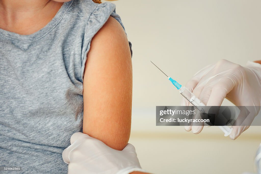 Doctor vaccinating small redhead girl.