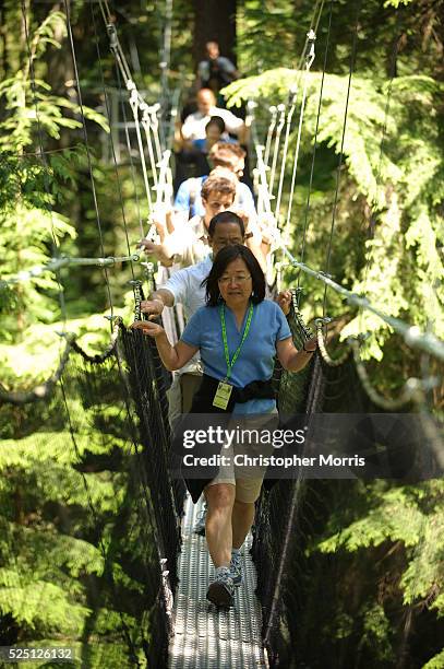 Woman walks with a group across the Greenheart Canopy Walkway at UBC Botanical Garden on the campus of the University of British Columbia. The...