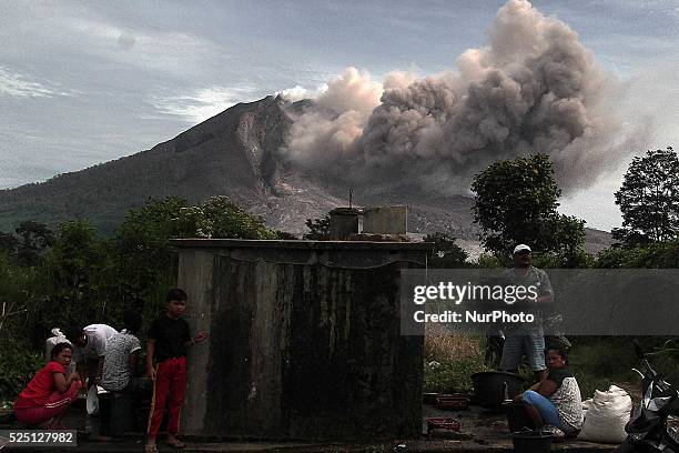 Residents washing clothes in a public water collection with the background of Mount Sinabung ejects clouds of hot clouds and volcanic ash from the...