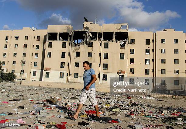 Palestinian man walks between clothes and rubble scattered on the ground in front of a destroyed house following an Israeli airstrike in Beit Lahiya,...