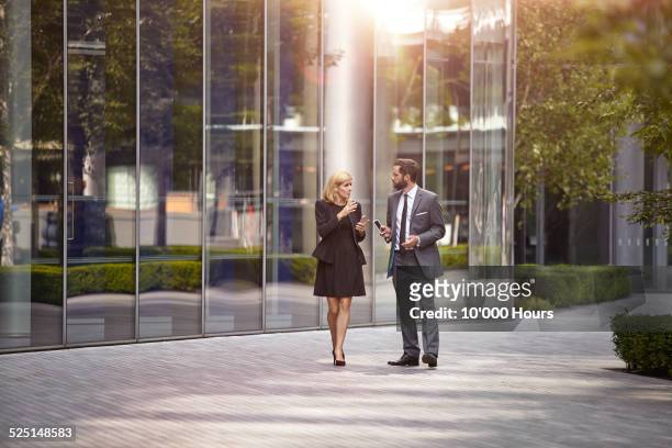 two coworkers walking and talking - business man woman walking stock-fotos und bilder
