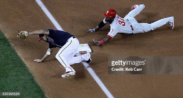Odubel Herrera of the Philadelphia Phillies slides safely into third on a passed ball as Anthony Rendon of the Washington Nationals bobbles the ball...