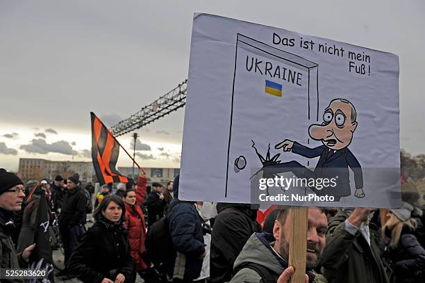 Demonstrator hold a caricature of Putin at rally called Friedenswinter at in Berlin, Germany in the air while the Sankt-Georgs-Flag is flying in the...