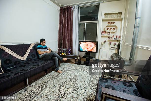 Iranian student Amir watching satellite Turkish TV channel, European or Turkish TV is forbidden, but common in modern Iranian houses, Isfahan, Iran