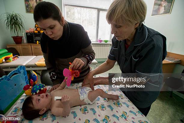 Mother, refuge from Gorlivka city in ATO region, calms down her disabled baby while getting massage therapy, Orphanage 'Zhytomyr regional children's...