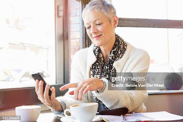 senior woman checks messages on phone in cafe. - cafe window stock pictures, royalty-free photos & images