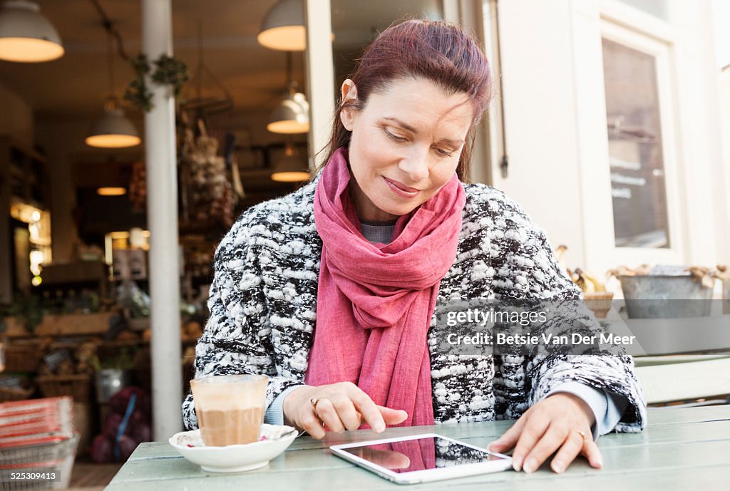 Mature woman looks at tablet computer sitting outside cafe.