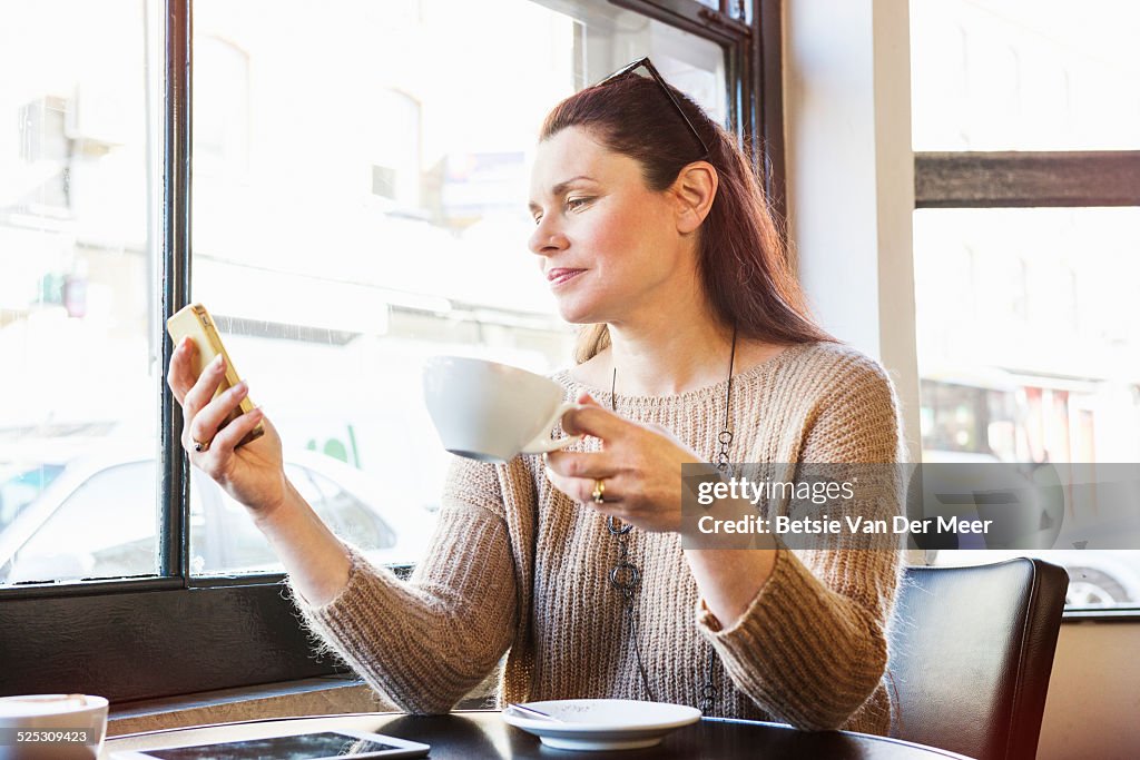 Senior women checks phone in cafe.