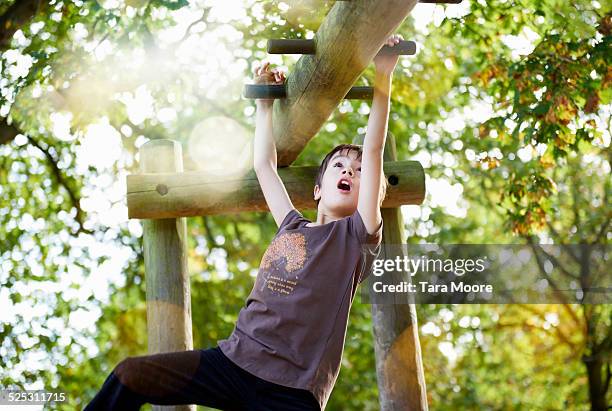 boy swinging on monkey bars in park - boy on monkey bars stock pictures, royalty-free photos & images