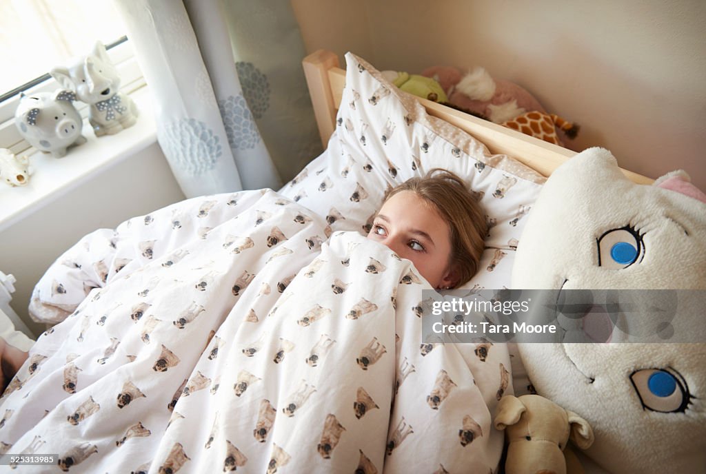 Teenage girl in bed peeking out from blanket