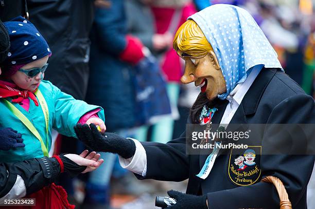 Participant with mask distributes sweets to a young girl during the traditional Rose Monday carnival parade on February 16, 2015 in Freiburg Germany.