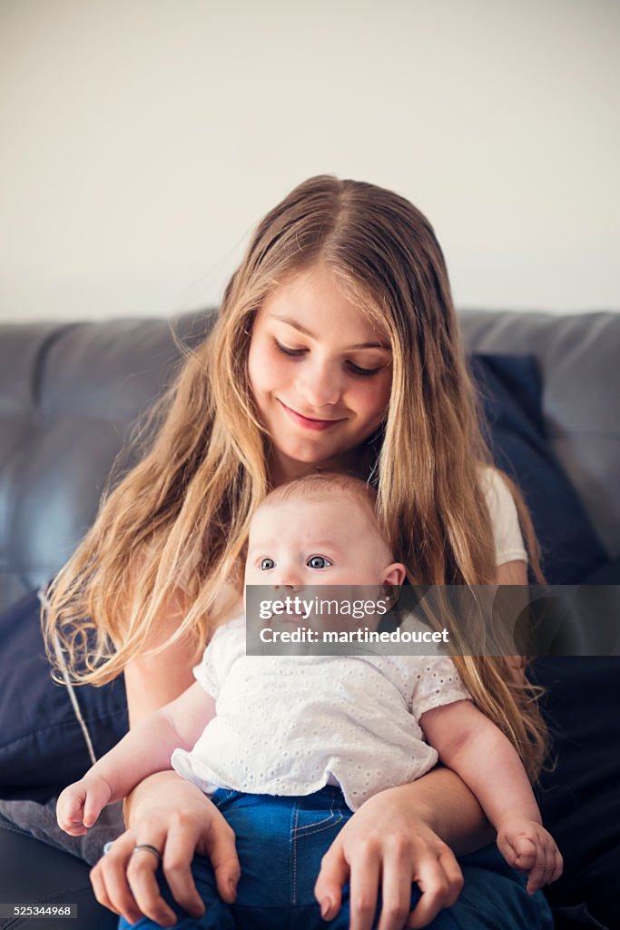 Un instant de tendresse entre grande sœur et bébé sur le canapé en famille.