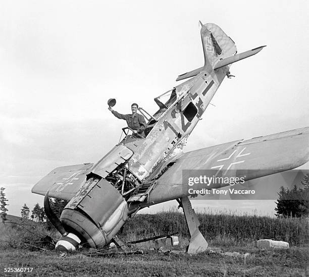 Is seen waving from the cockpit of a downed German Focke-Wulf Fw 190 fighter aircraft, Pocking, Bavaria, Germany, World War II, July 1945.