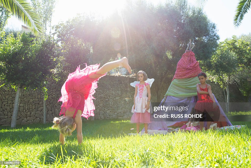 Girls watching friend in fairy costume doing handstand in garden