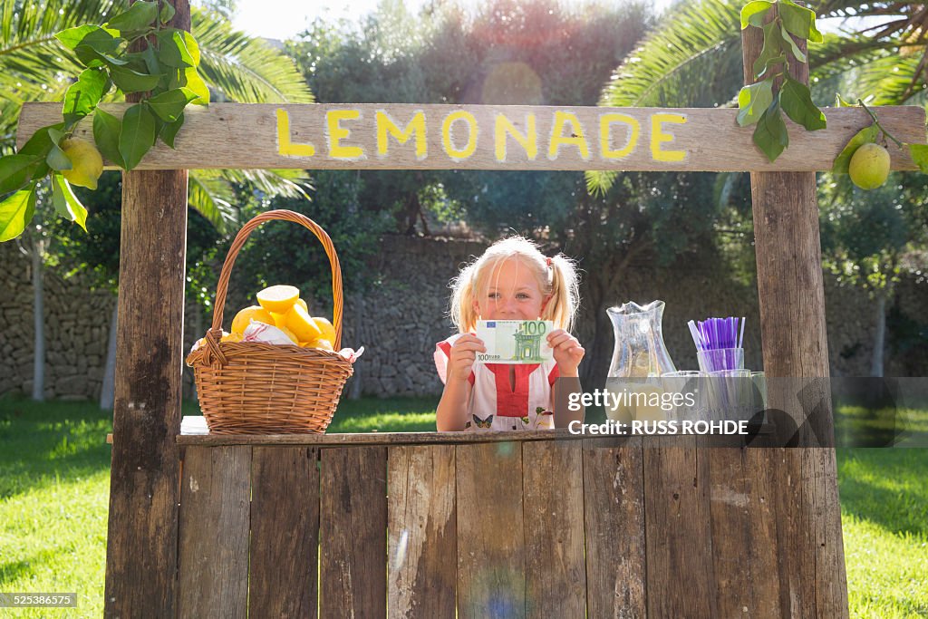 Portrait of girl on lemonade stand holding up one hundred euro note