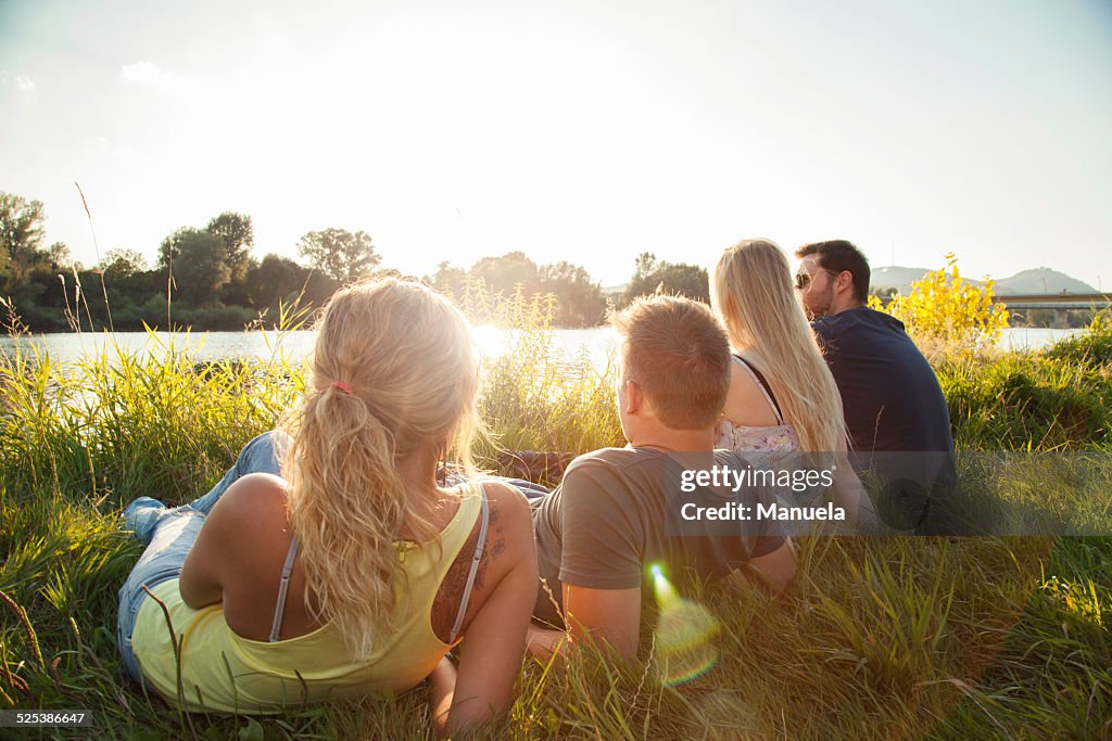 Four young adult friends reclining on riverbank