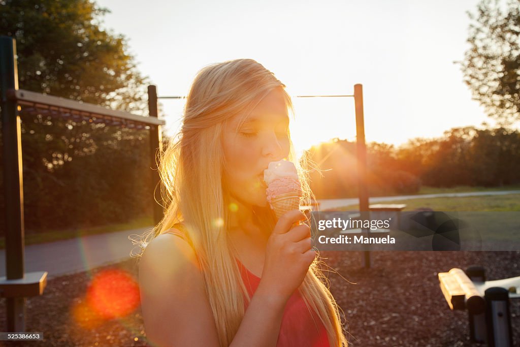 Young woman eating ice cream cone in park at sunset