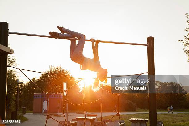 silhouetted young woman upside down on playground climbing frame at sunset - climbing frame stock pictures, royalty-free photos & images