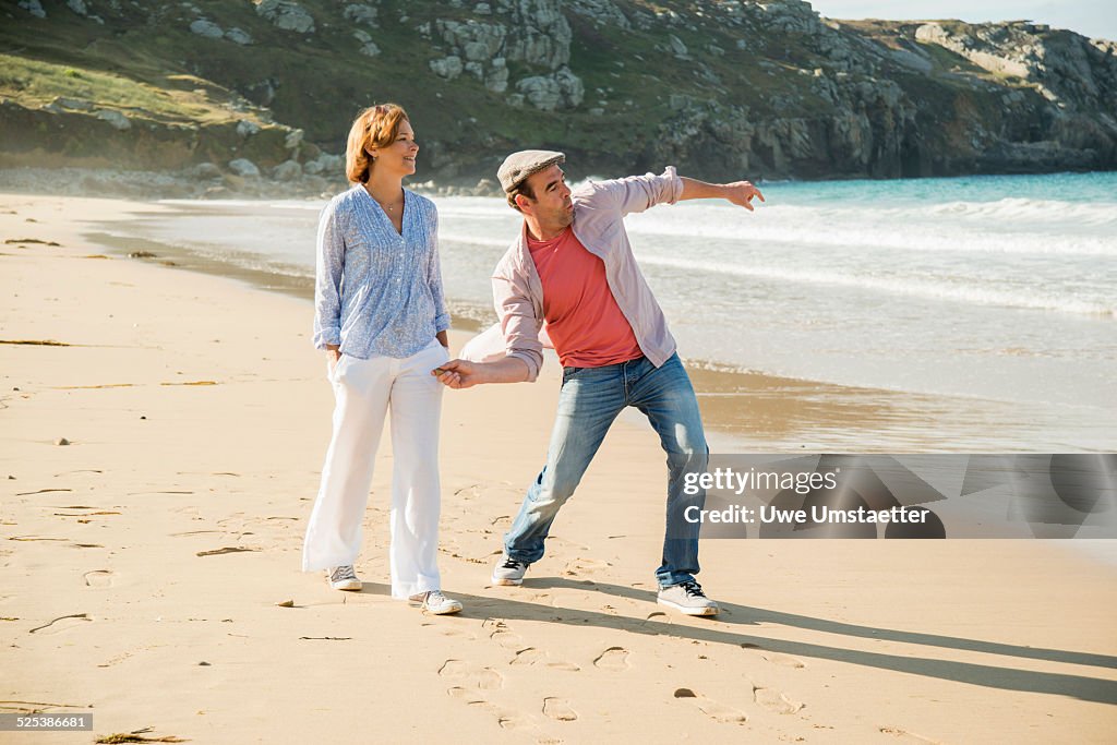 Mature couple throwing pebbles out to sea, Camaret-sur-mer, Brittany, France