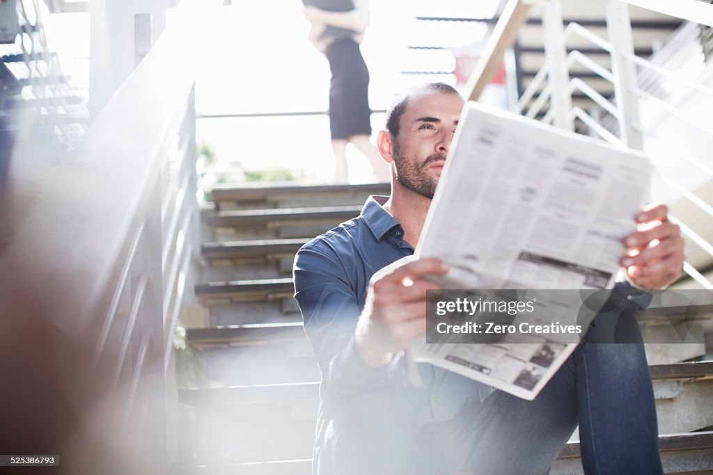 Businessman reading newspapers on staircase
