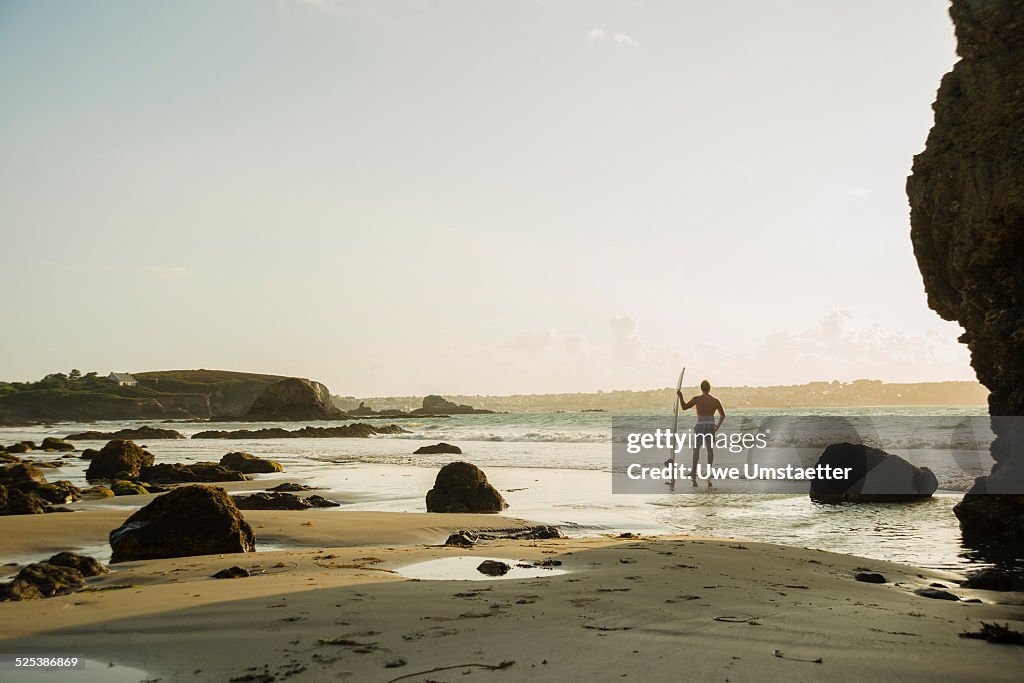 Mature man standing at waters edge holding surf board