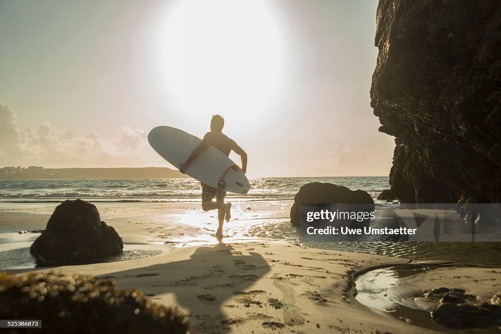 Mature man running towards sea, holding surf board