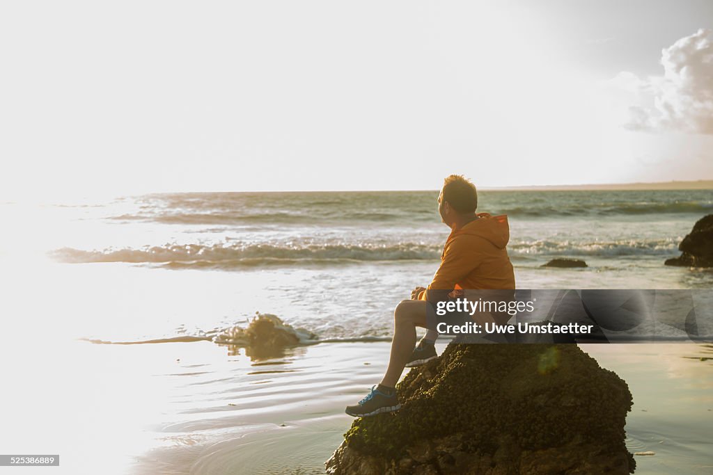 Mature man, sitting on rock, looking out to sea