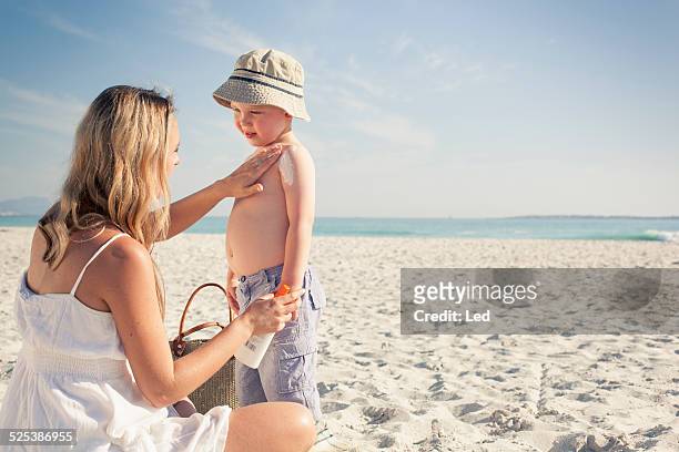 mid adult mother applying sun lotion to young son on beach, cape town, western cape, south africa - applying sunscreen stock pictures, royalty-free photos & images