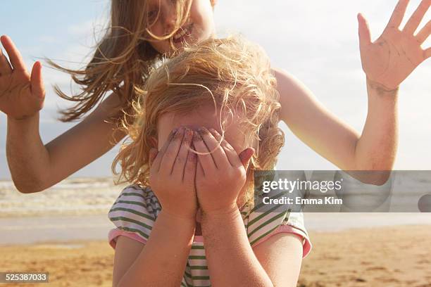 girl covering eyes in front of sister on beach, camber sands, kent, uk - camber sands stockfoto's en -beelden