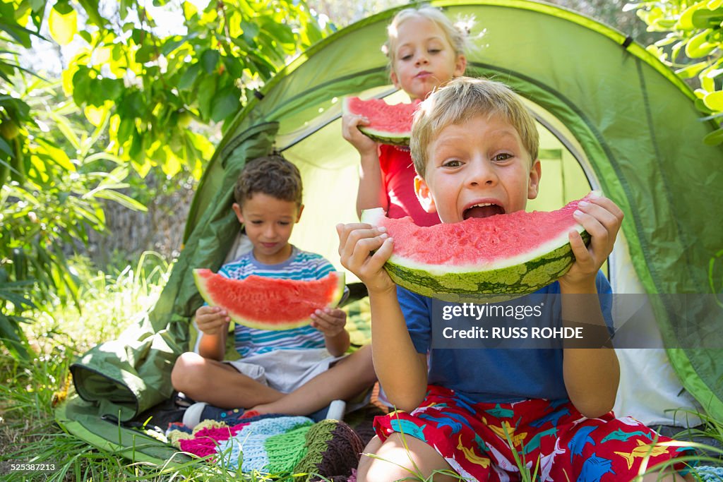 Three children eating large watermelon slices in garden tent