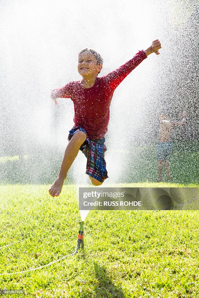 Boy jumping over water sprinkler in garden