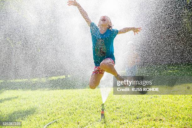 girl jumping over water sprinkler in garden - girl wet casual clothing stock pictures, royalty-free photos & images