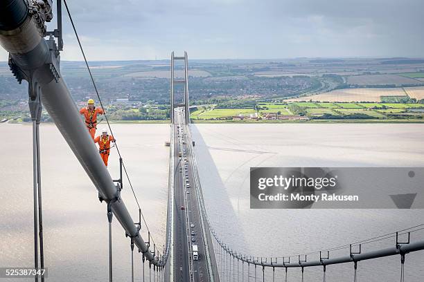 bridge workers walking on cable of suspension bridge. the humber bridge, uk was built in 1981 and at the time was the worlds largest single-span suspension bridge - humber bridge stock-fotos und bilder