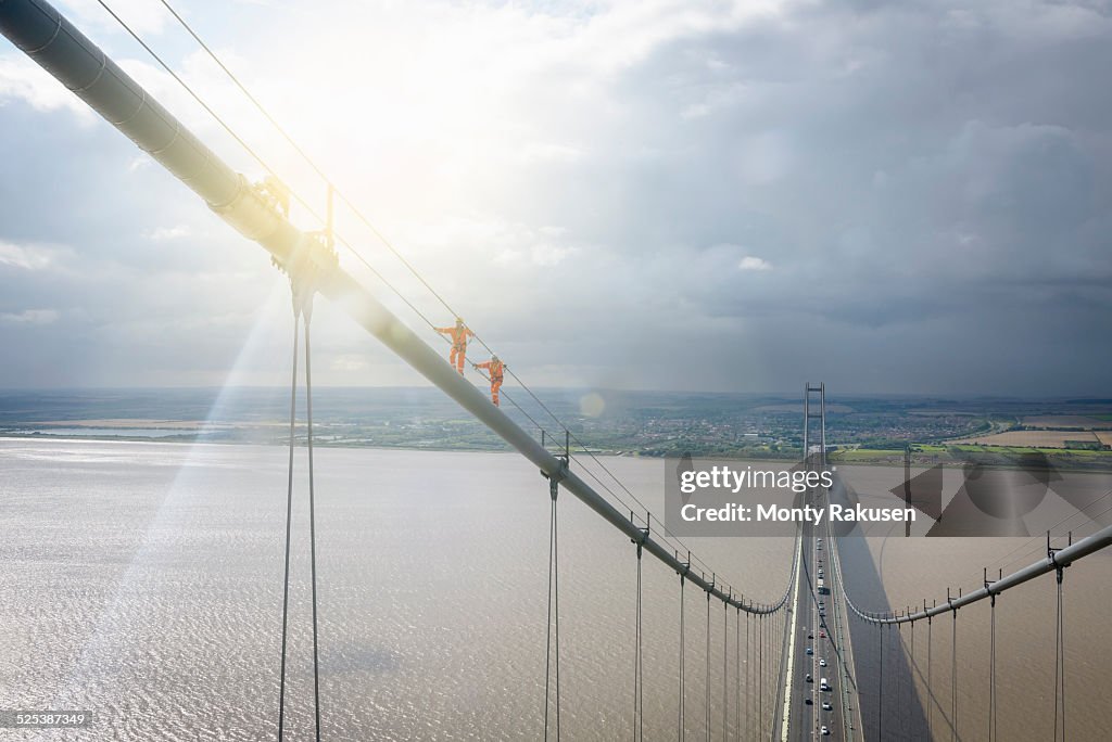 Bridge workers walking on cable of suspension bridge under bright sunlight. The Humber Bridge, UK was built in 1981 and at the time was the worlds largest single-span suspension bridge